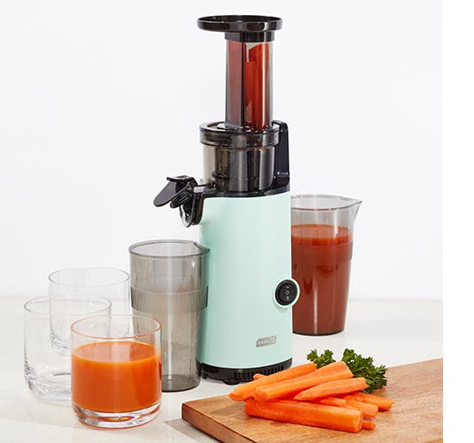 A juicer surrounded by glasses and vegetables.