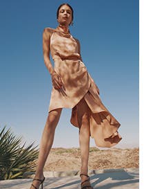A model in an off-white dress standing in the desert.