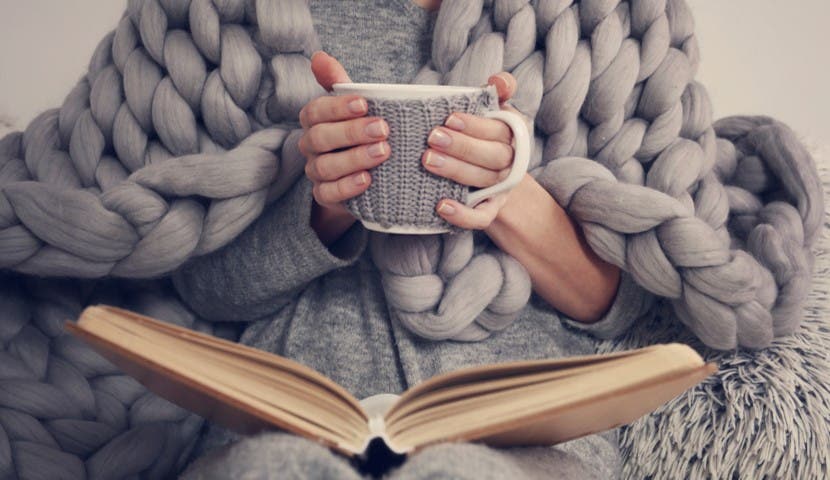 weighted blanket wrapped around a woman with cup of coffee and a book