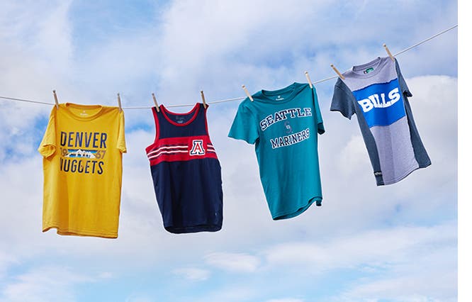 Four T-shirts and tanks with team logos hanging on a clothesline.