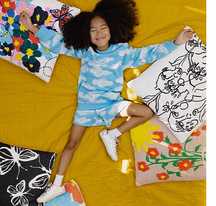 A girl surrounded by embroidered accent pillows.
