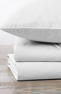 A white pillow on top of folded bed sheets.