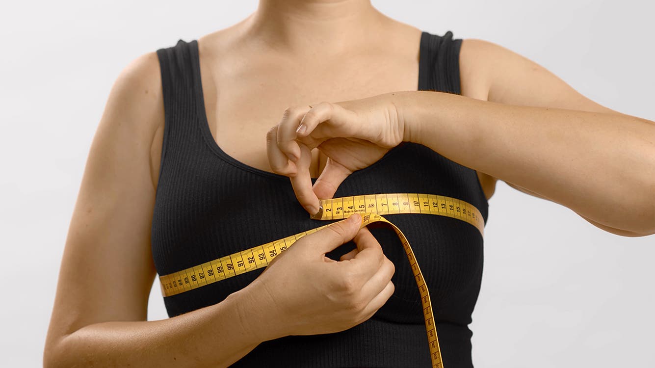 A woman uses a measuring tape to measure her bust.