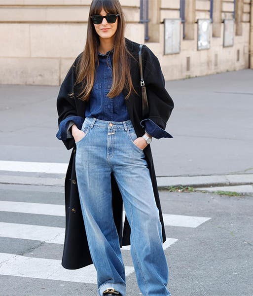 A woman wearing wide-leg jeans, a darker denim shirt tucked in and a long, dark coat.