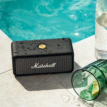 A portable Marshall Bluetooth speaker beside a swimming pool.