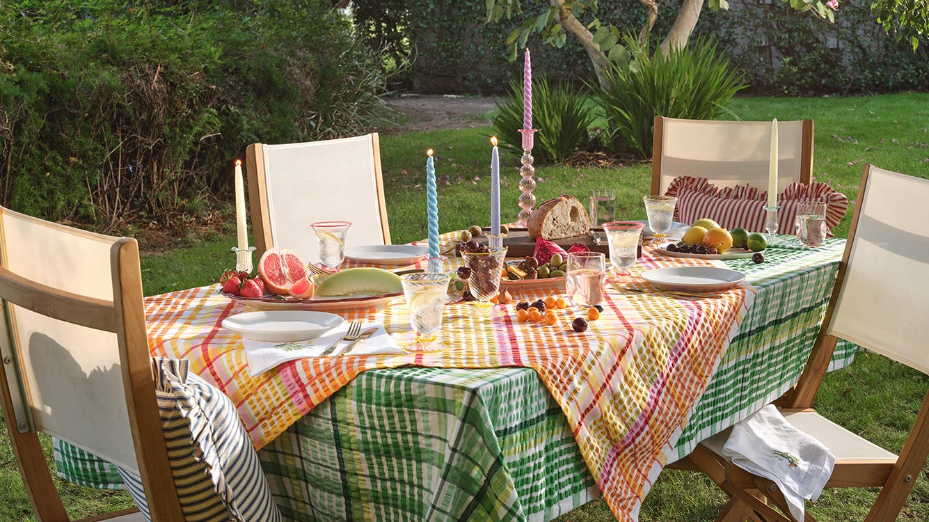 An outdoor dining table set with layered tablecloths, colorful dishware and jewel-toned candleholders.