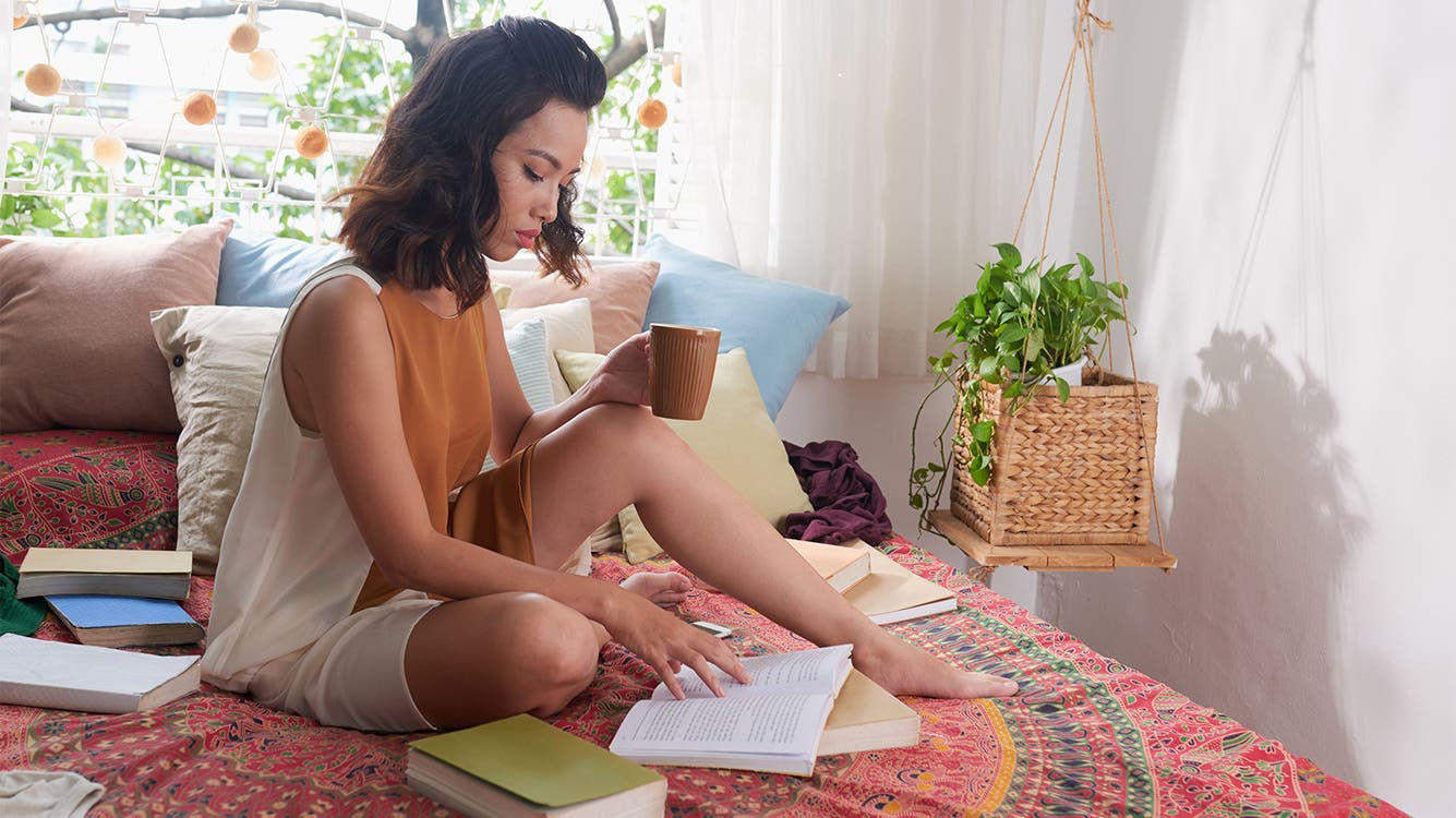 A young woman reading a book on a bed.