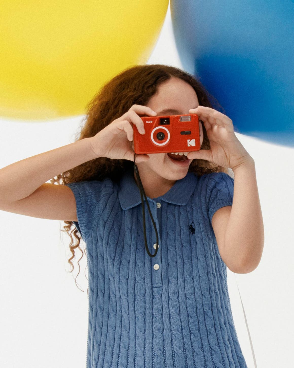 A girl in a knit polo holding a camera.
