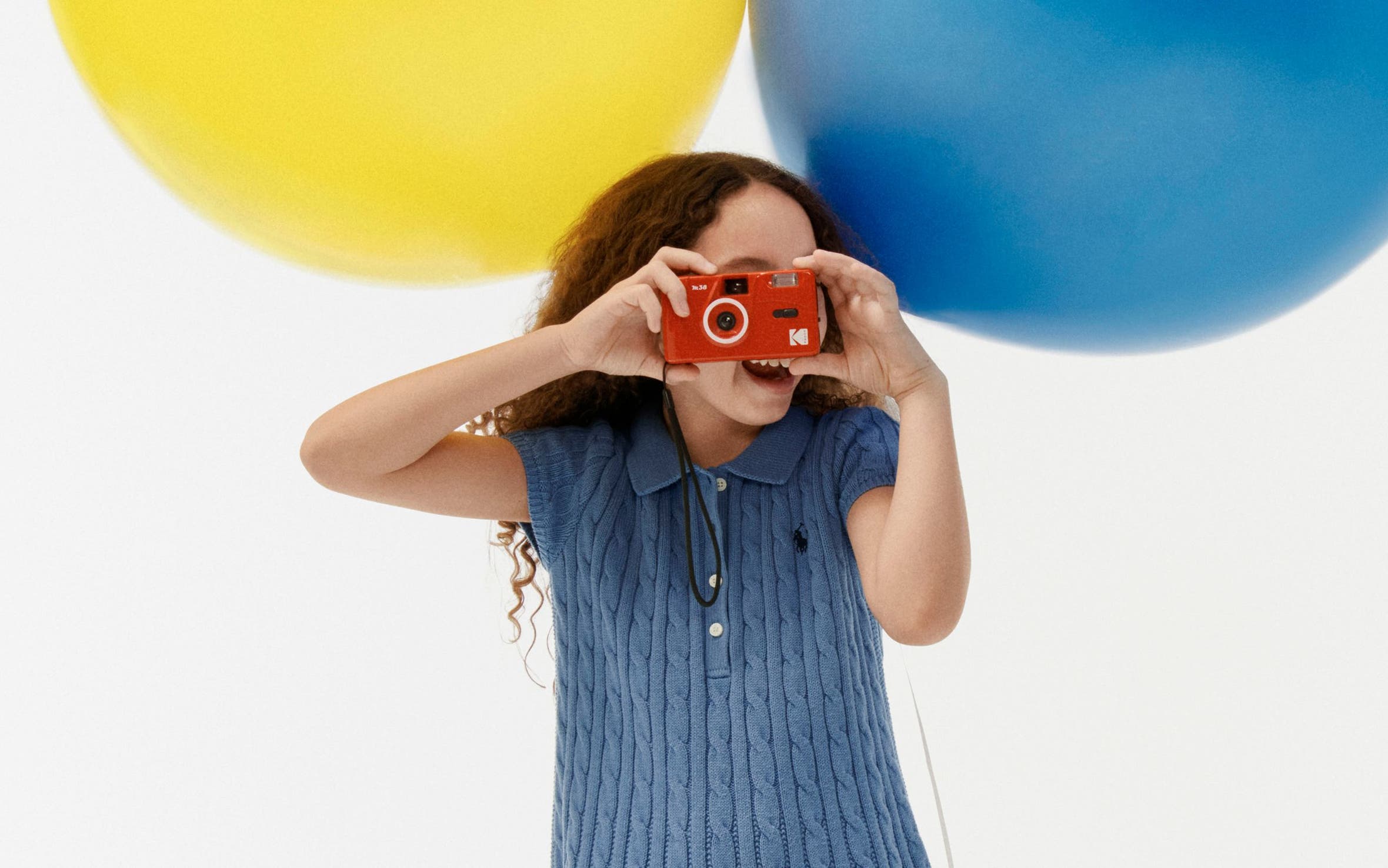 A girl in a knit polo holding a camera.