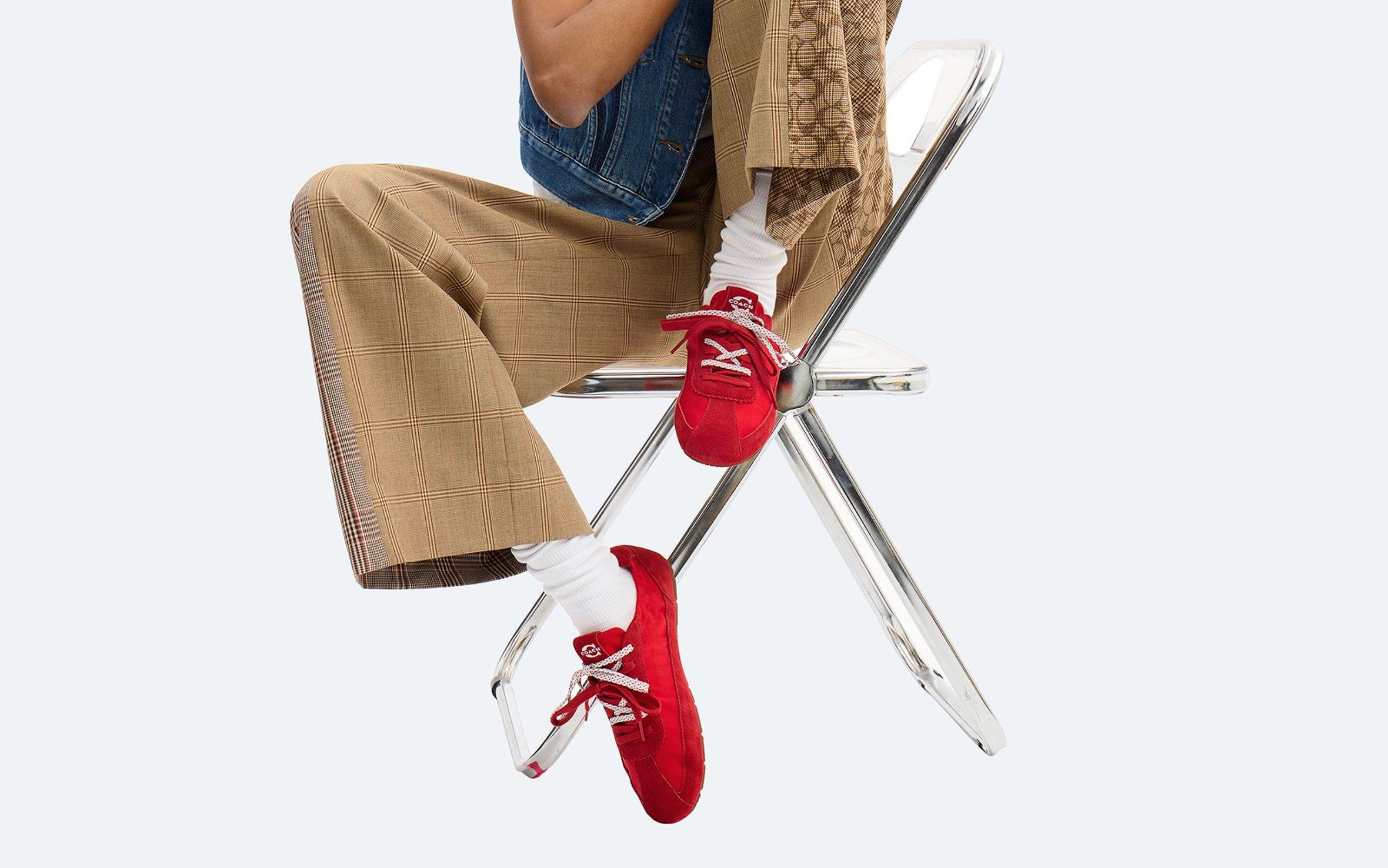 A girl sitting on a chair wearing red COACH sneakers with double laces