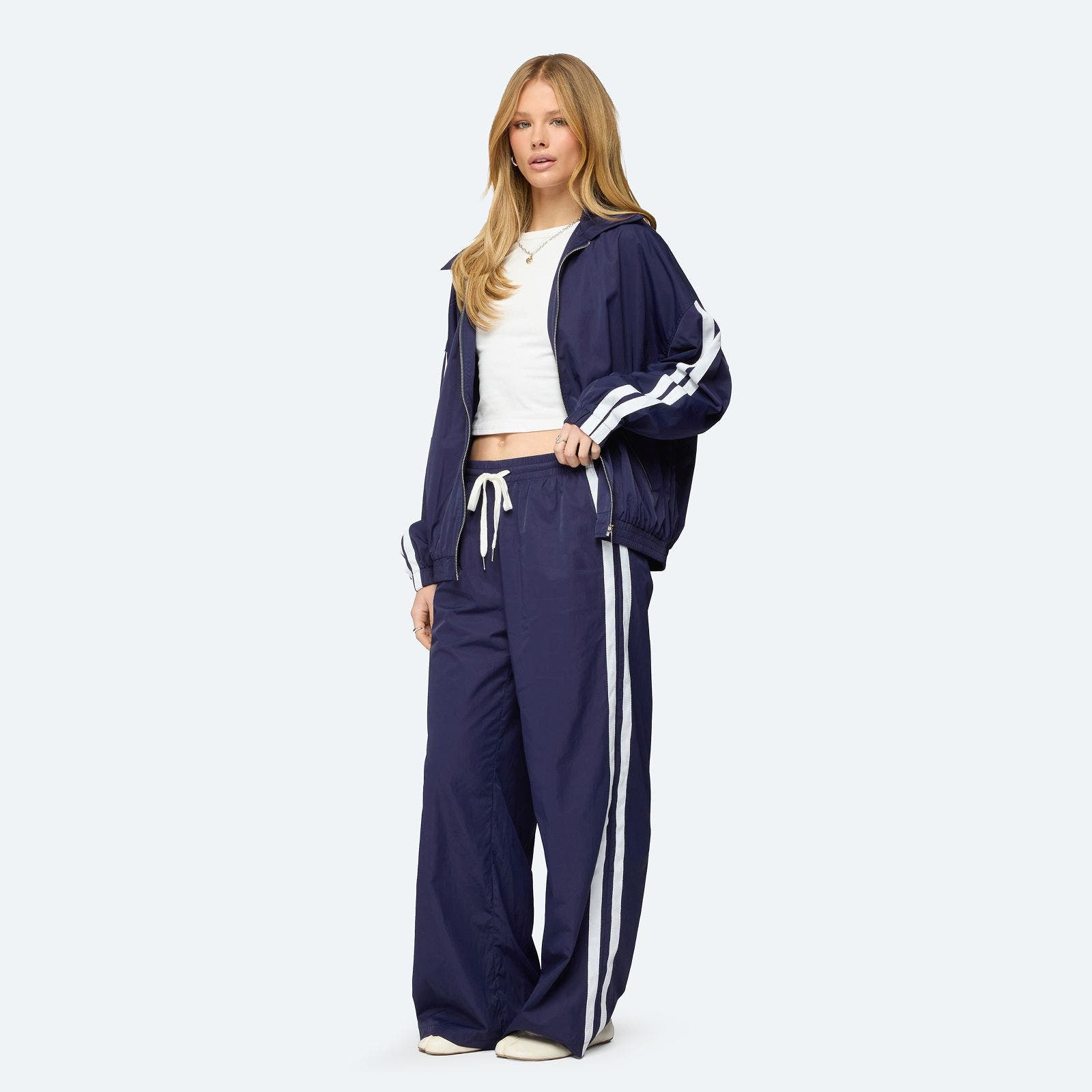 A woman in an oversized navy track suit and white shirt. 
