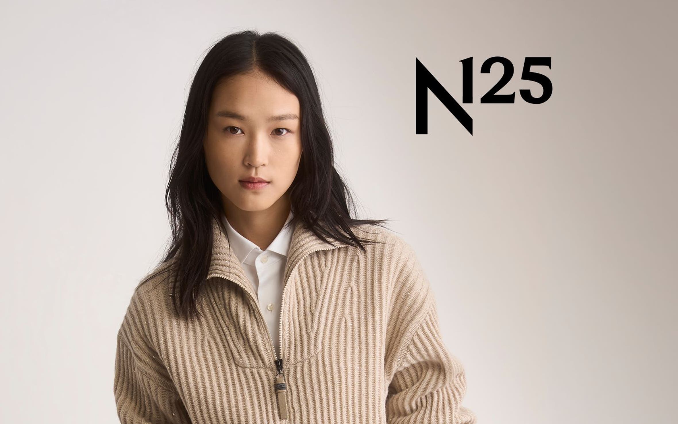 A woman in a camel ribbed zip cardigan, white shirt and cream pants.