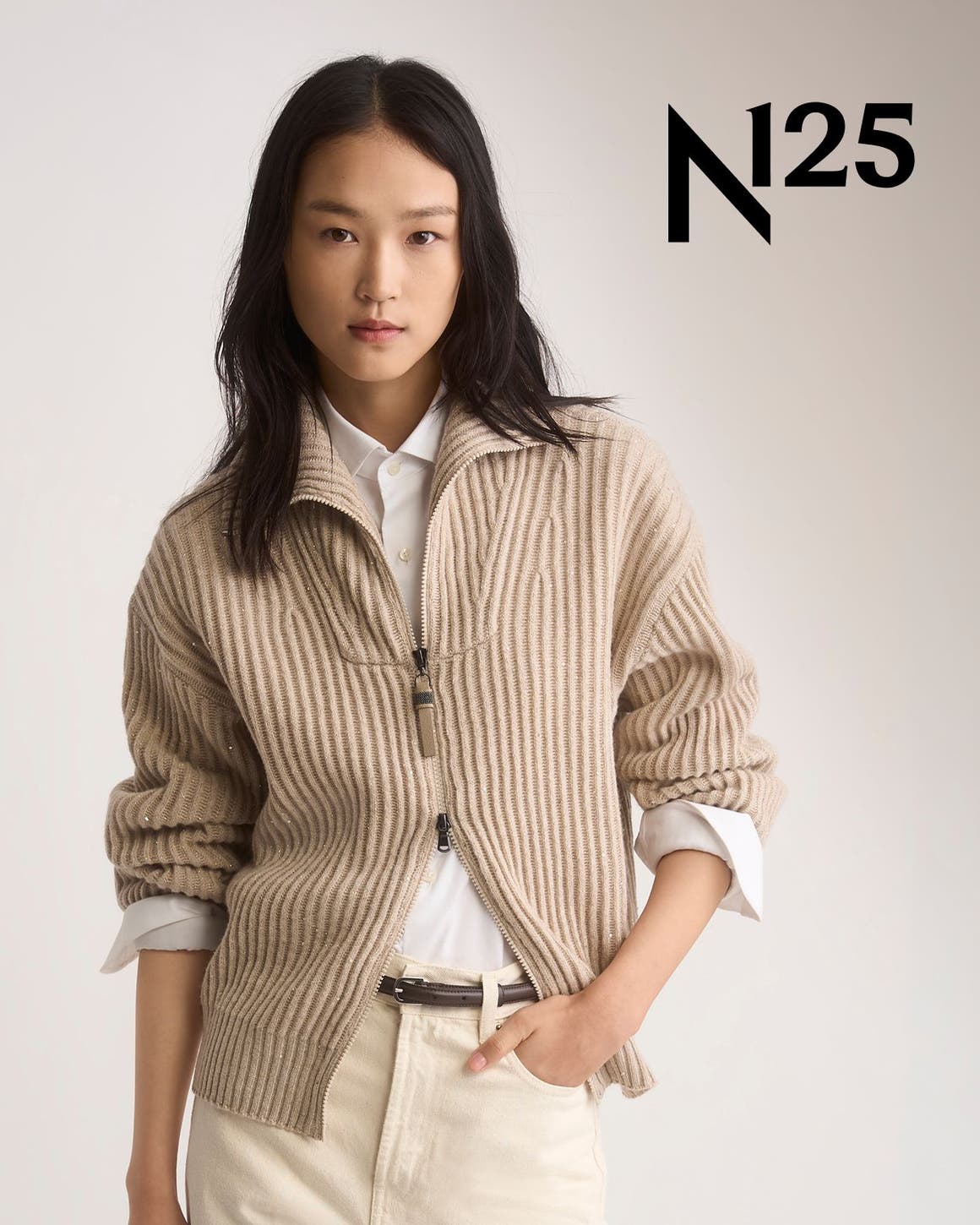 A woman in a camel ribbed zip cardigan, white shirt and cream pants.