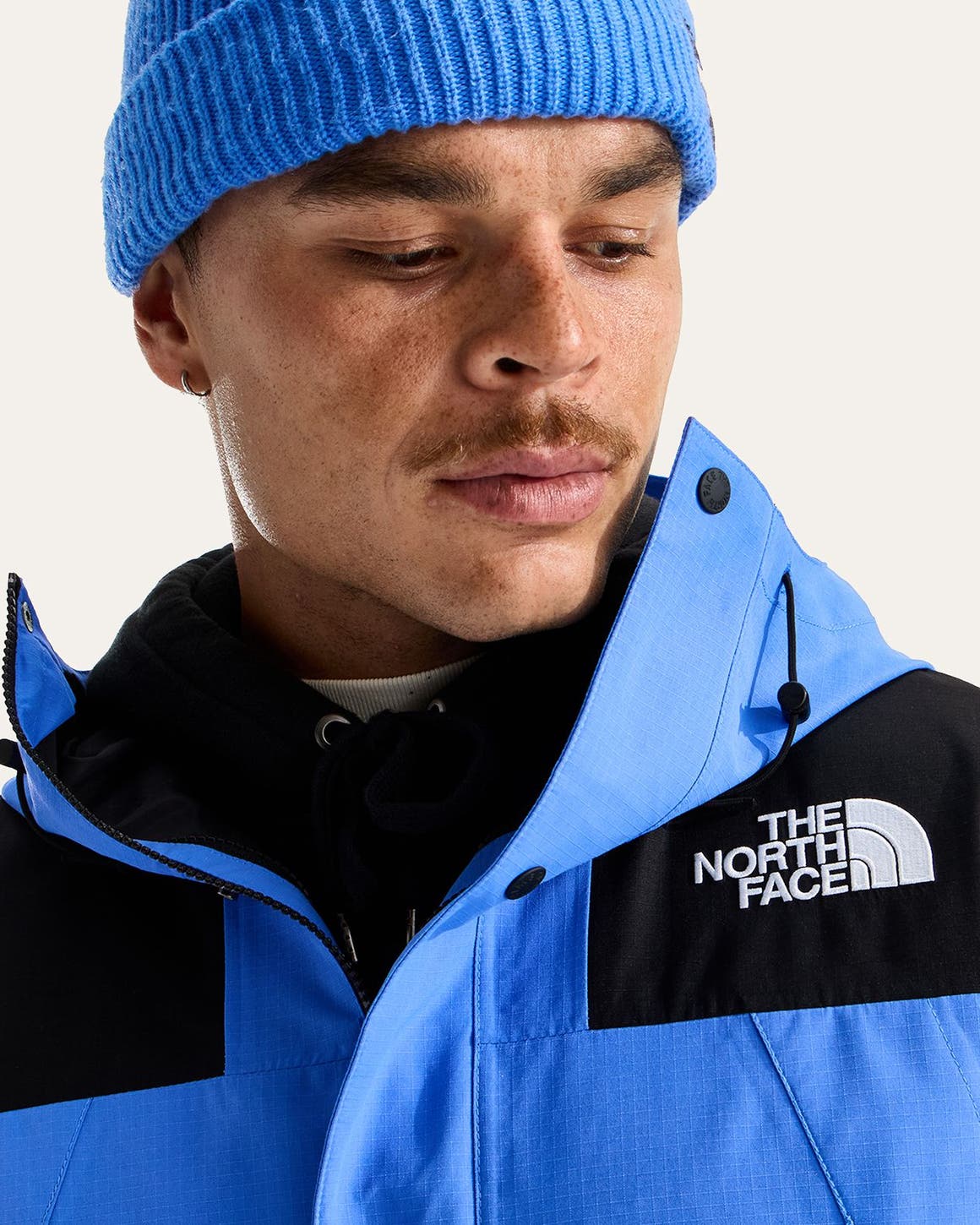 A man in a blue The North Face jacket with black panels and a blue knit beanie.