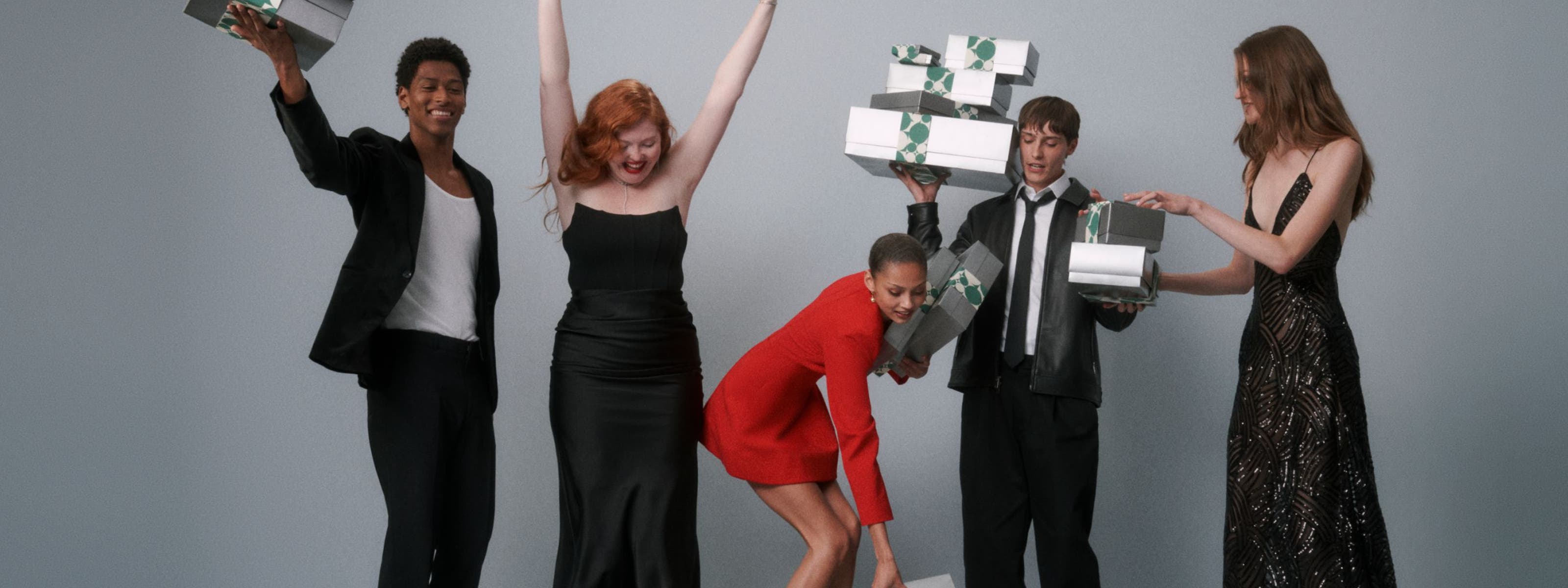 A group of people in formal dress holding silver Nordstrom gift boxes.