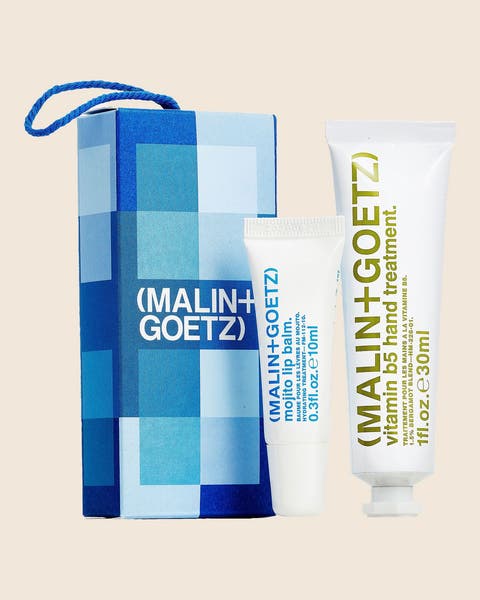 A MALIN+GOETZ gift set with a vitamin B5 hand treatment tube and a lip balm beside a blue checkered box.