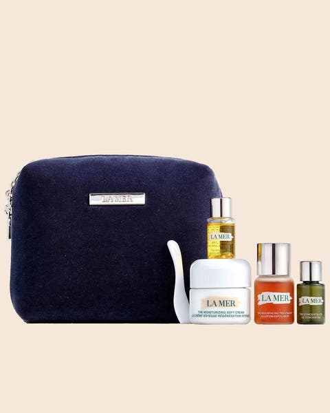 A navy zip pouch with a La Mer cream, a dropper oil and two travel-size bottles.