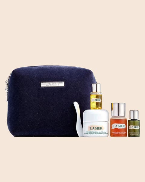 A La Mer skincare set with a navy velvet pouch, a cream jar and three small serum and oil bottles.
