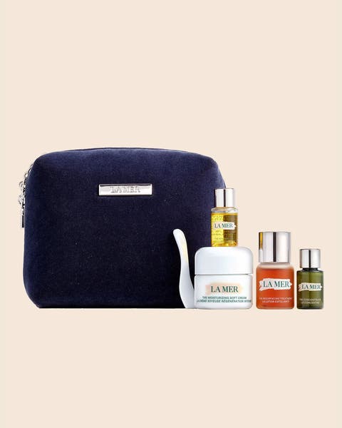 A navy zip pouch with a La Mer cream, a dropper oil and two travel-size bottles.