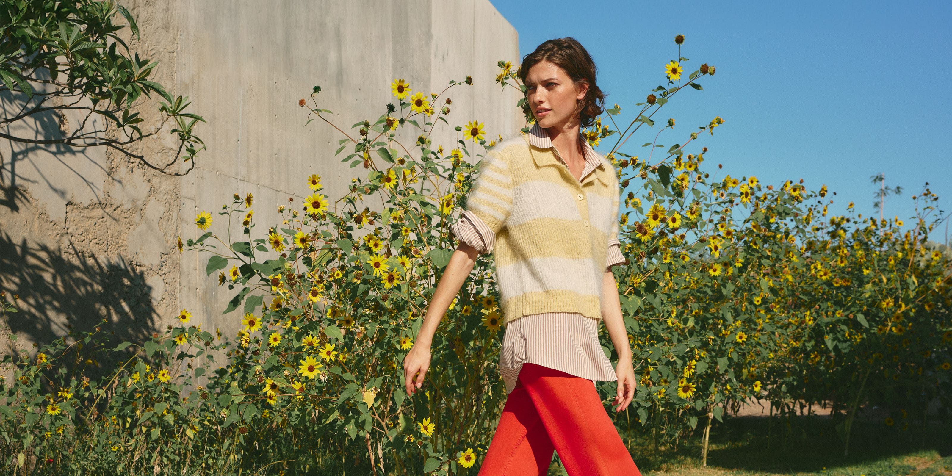 A woman wearing a yellow striped sweater, button up shirt, and red pants.