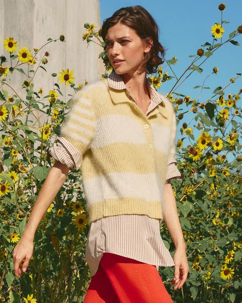 A woman wearing a yellow striped sweater, button up shirt, and red pants.