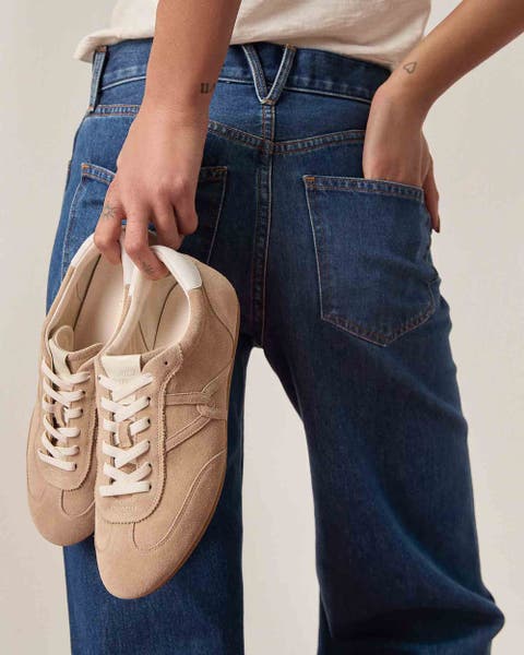 A woman wearing Veronica Beard jeans and holding a pair of sneakers from the brand. 