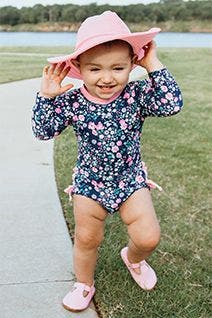 A baby in a sun-protective swimsuit and hat.