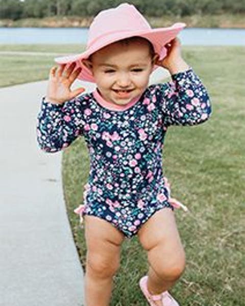 A baby in a sun-protective swimsuit and hat.
