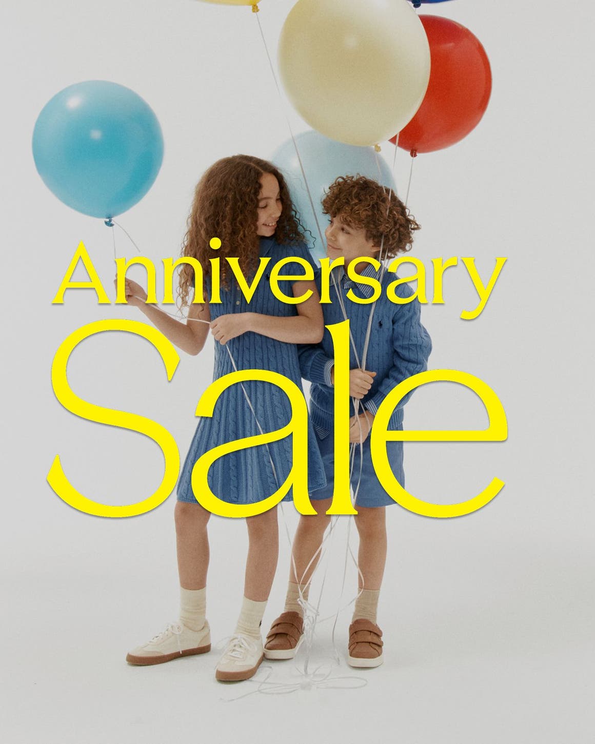 Girl and boy holding ballons with Anniversary Sale graphic