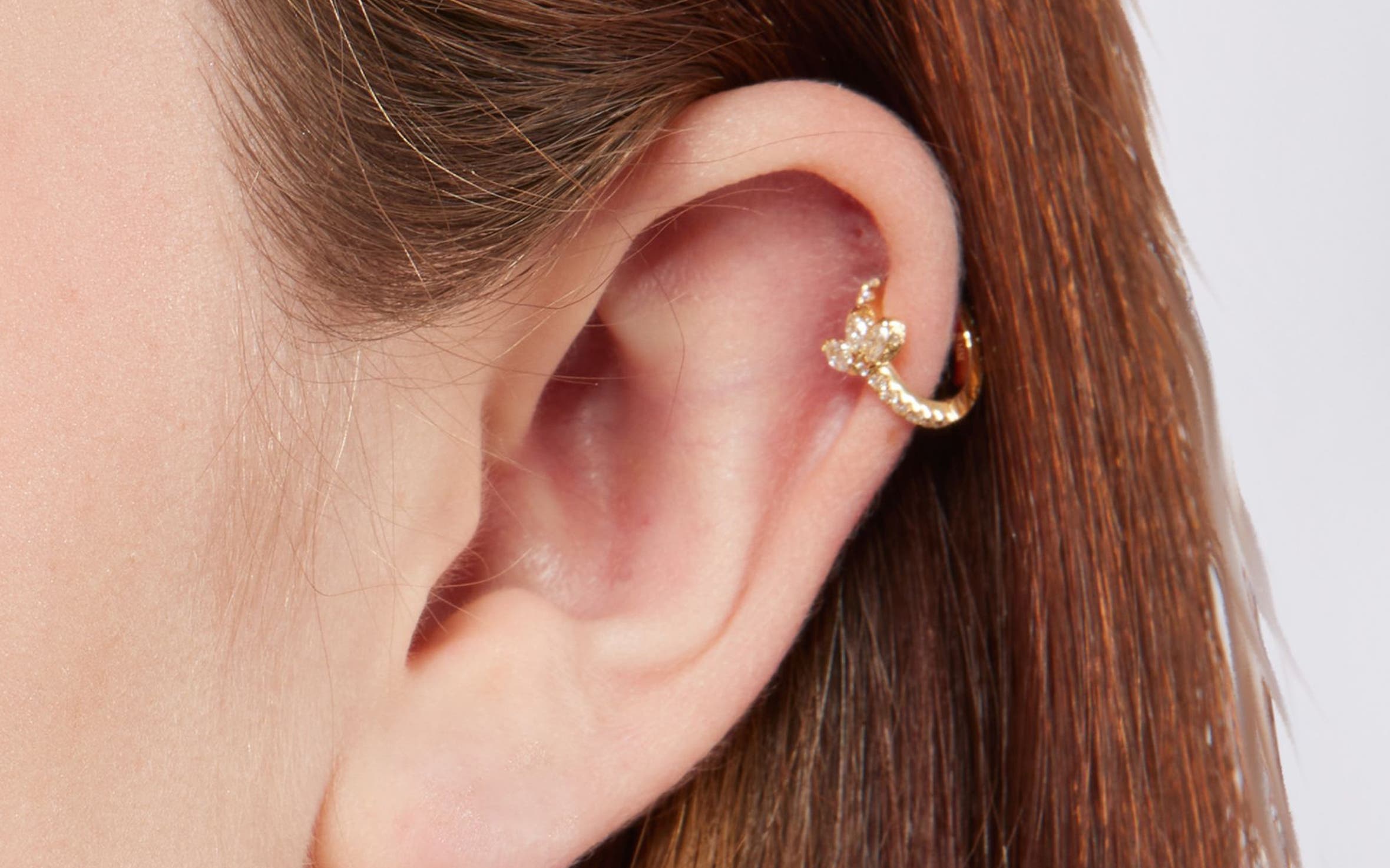 A woman with a helix ear piercing and gold ring.