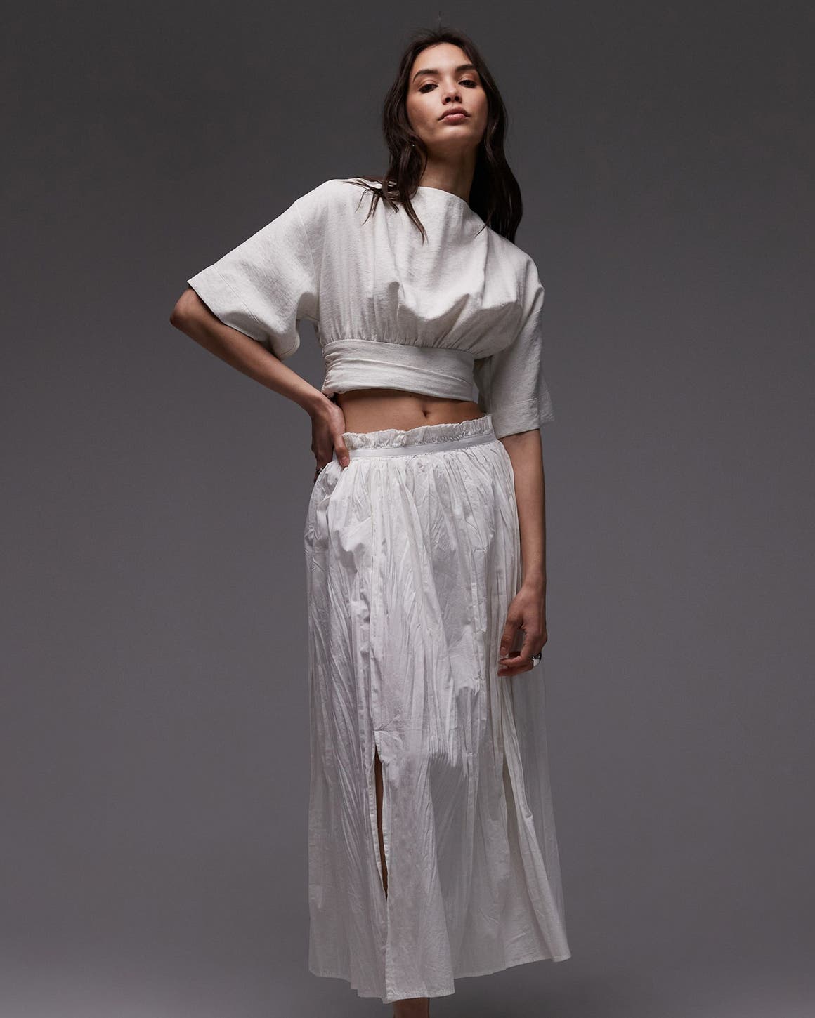 A woman in a white cropped top and flowing white skirt.