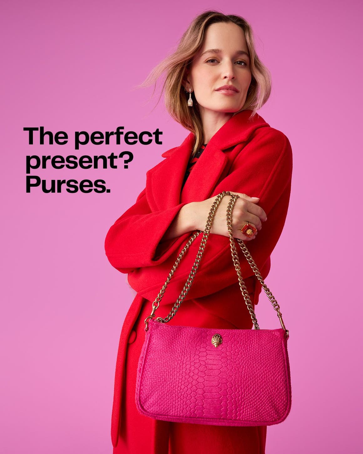 A woman wearing a red wool coat holding a hot pink Kurt Geiger London snakeskin print bag with chain strap. 