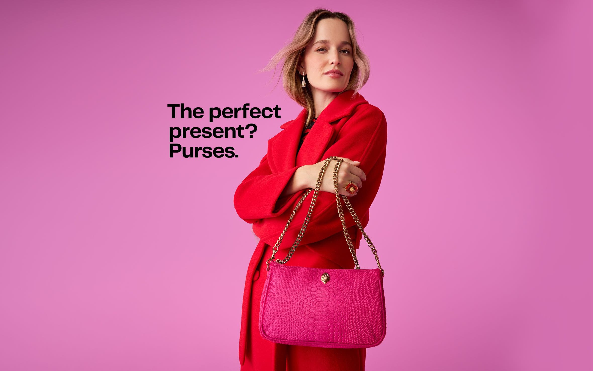 A woman wearing a red wool coat holding a hot pink Kurt Geiger London snakeskin print bag with chain strap. 