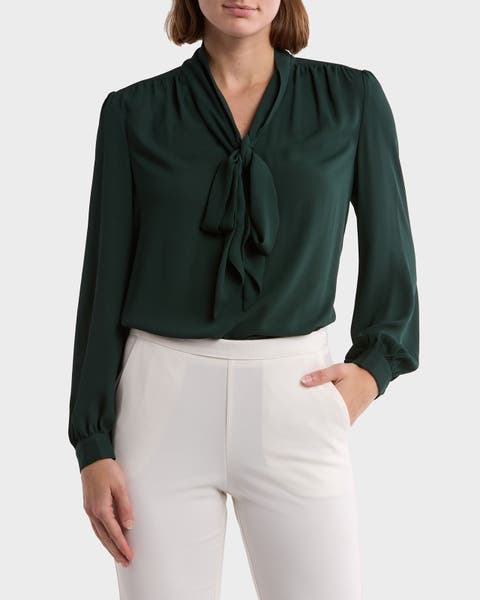 A woman wearing a green tie blouse with white pants.