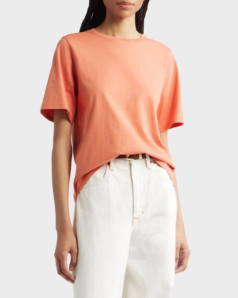 A woman wearing an orange tee with white jeans.