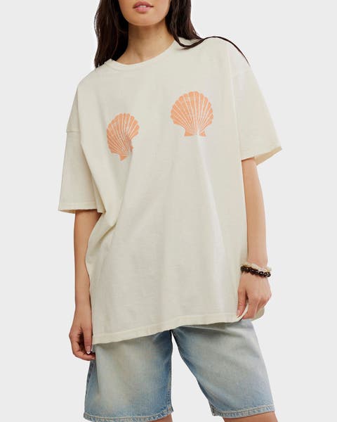 A woman wearing an oversized t-shirt with a seashell print and jeans.