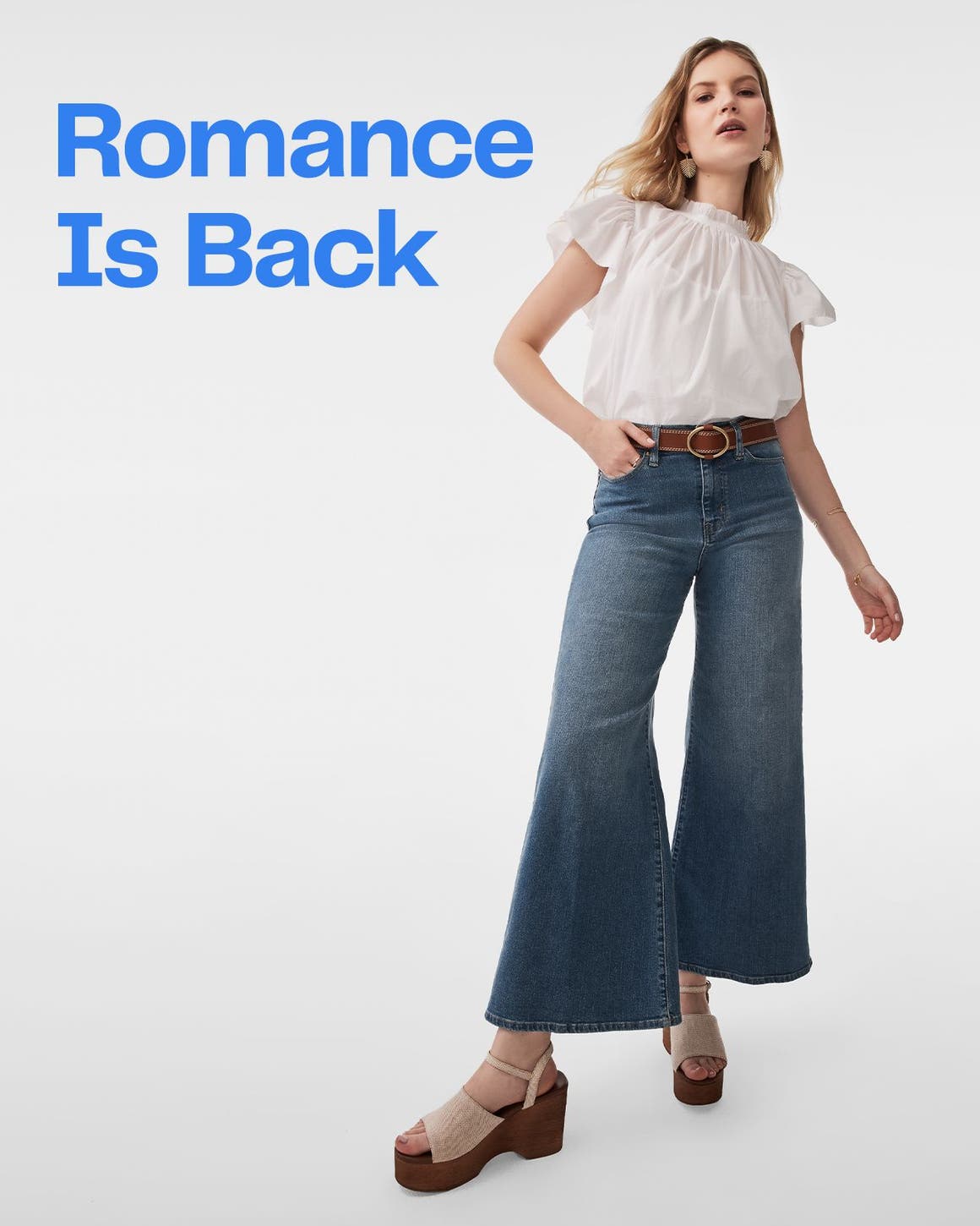 A woman wearing a white top, flared jeans and platform sandals.