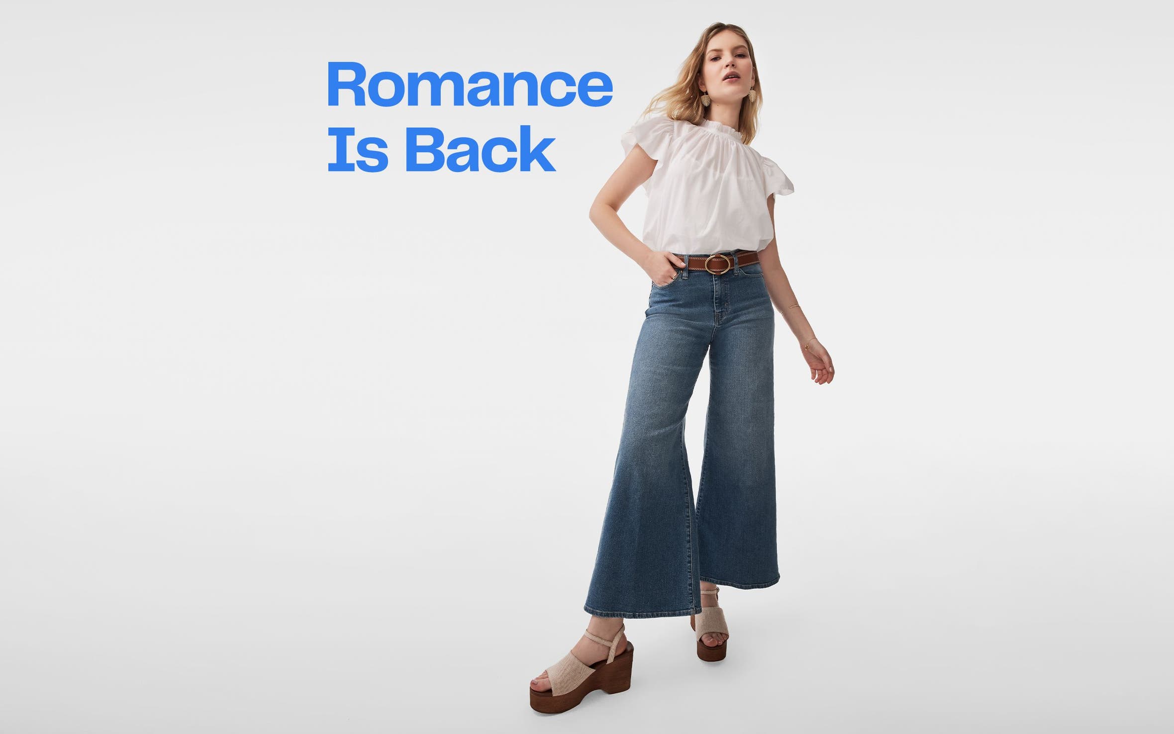 A woman wearing a white top, flared jeans and platform sandals.