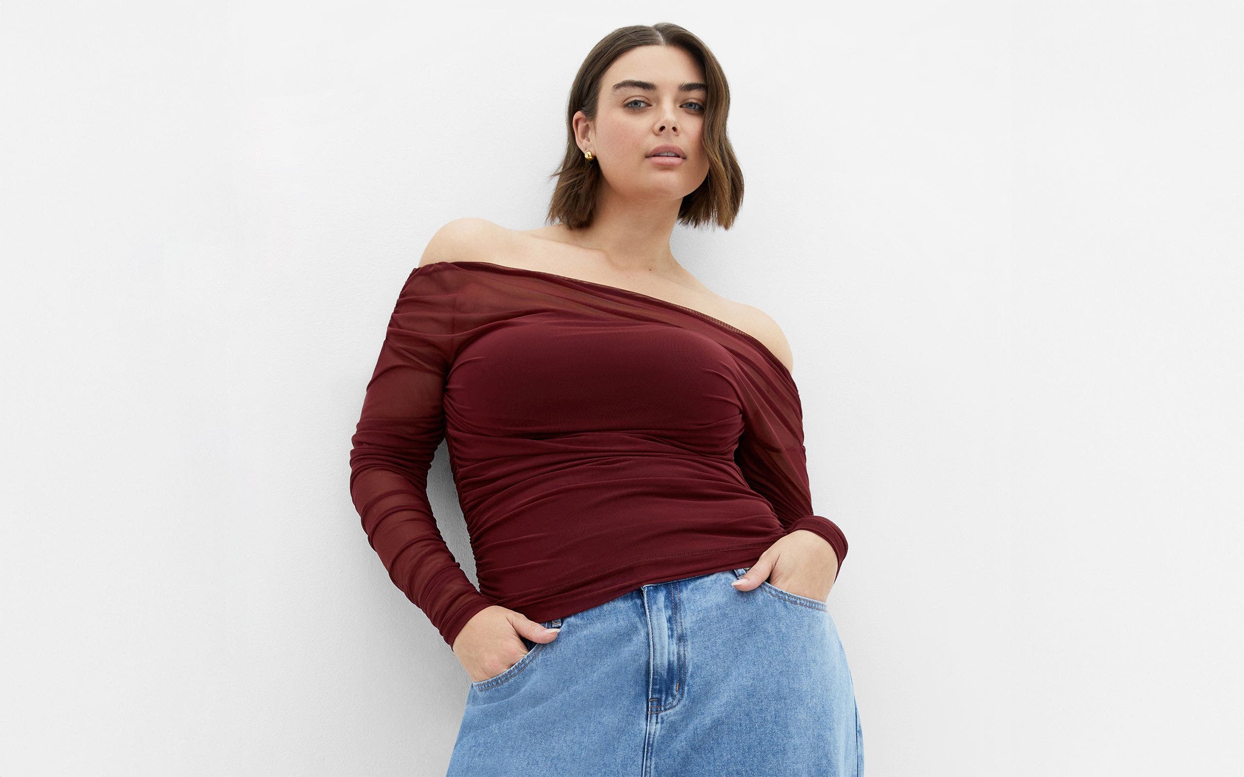 A woman wearing a burgundy off-the-shoulder top and denim