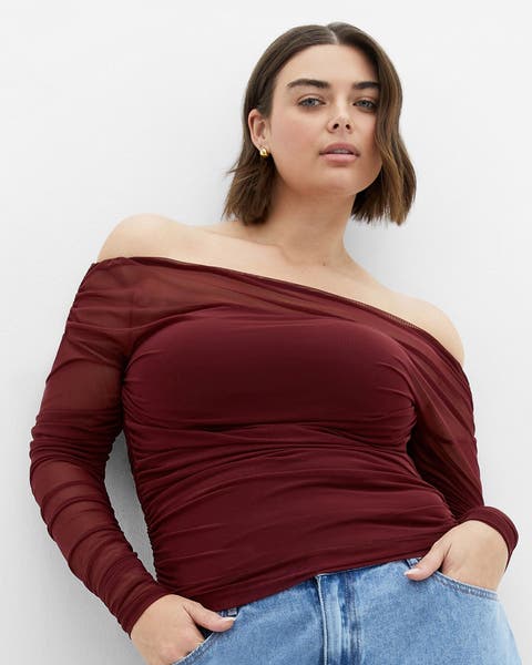 A woman wearing a burgundy off-the-shoulder top and denim