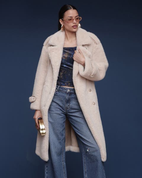 A woman wearing a knee length cream faux-fur jacket.