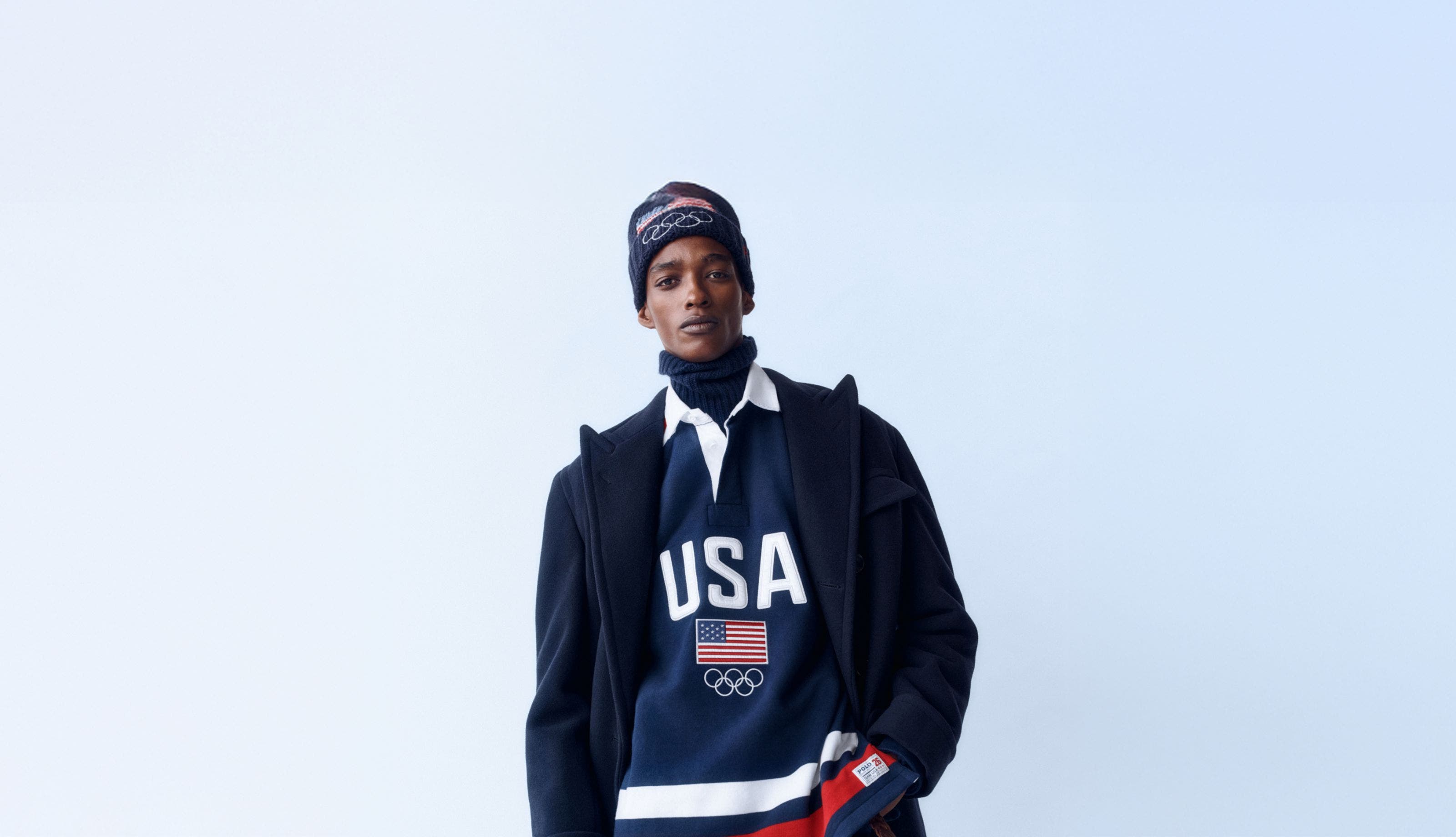 A man wearing a turtleneck, rugby shirt, coat and beanie from the Polo Winter Olympics collection.