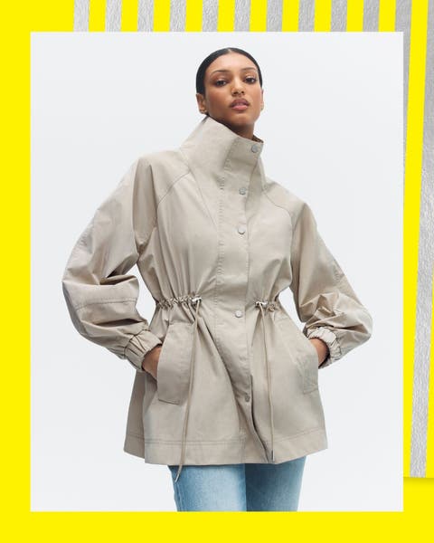A woman in an off-white, high-collar rain jacket, cinched at the waist.