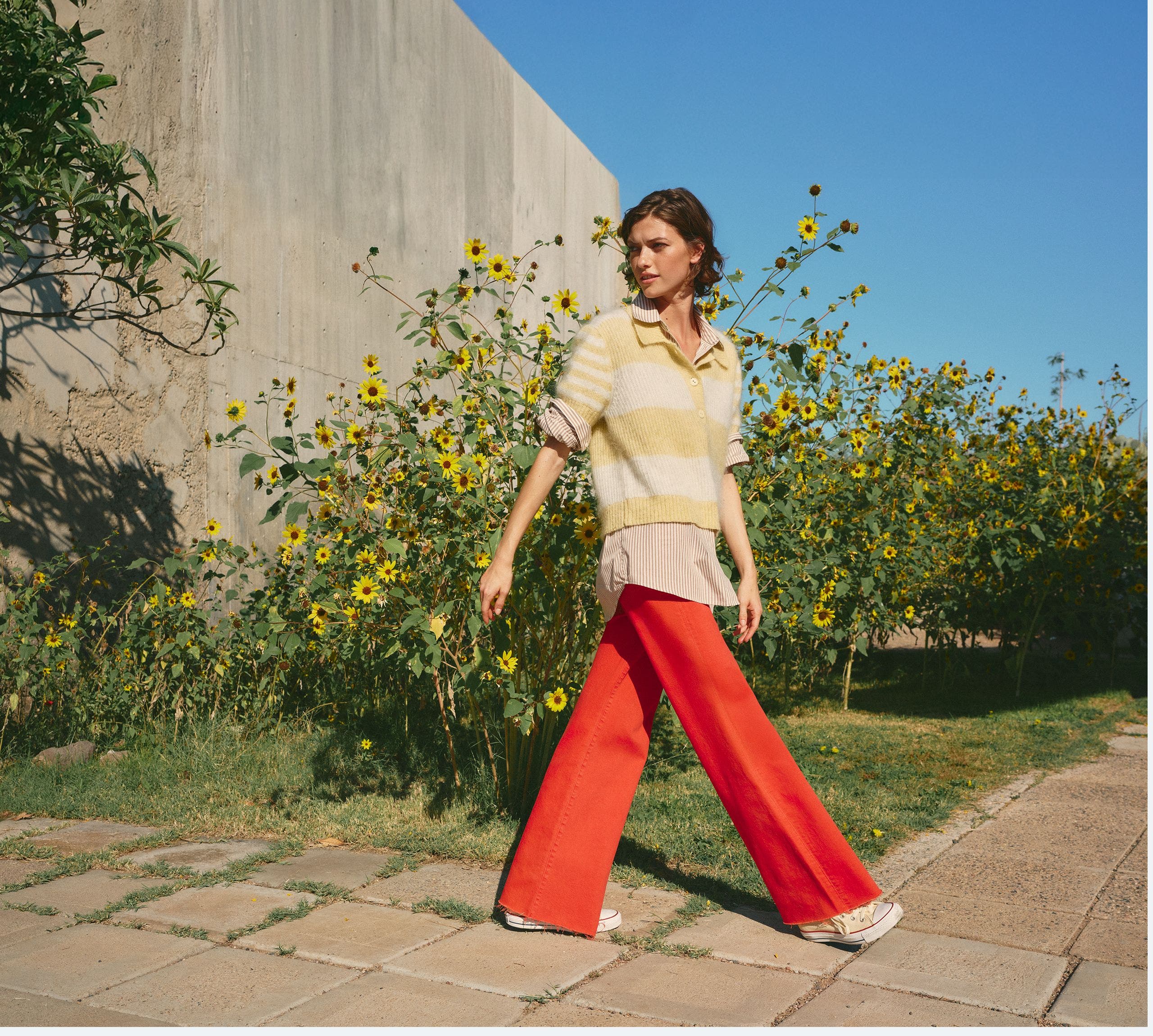 Woman wearing a striped sweater, button-up shirt and red pants.