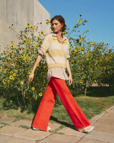 Woman wearing a striped sweater, button-up shirt and red pants.
