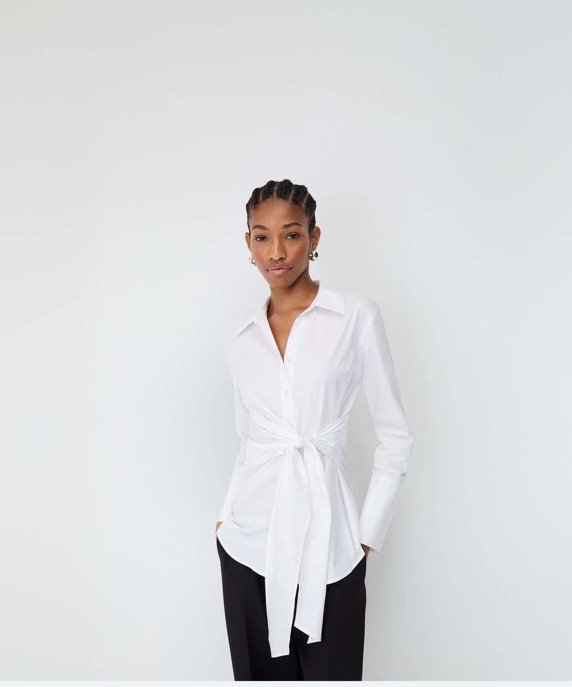 Woman wearing a white tie-front blouse and black pants.