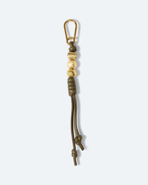 A bag charm with gold beads and a knotted green leather tassel.