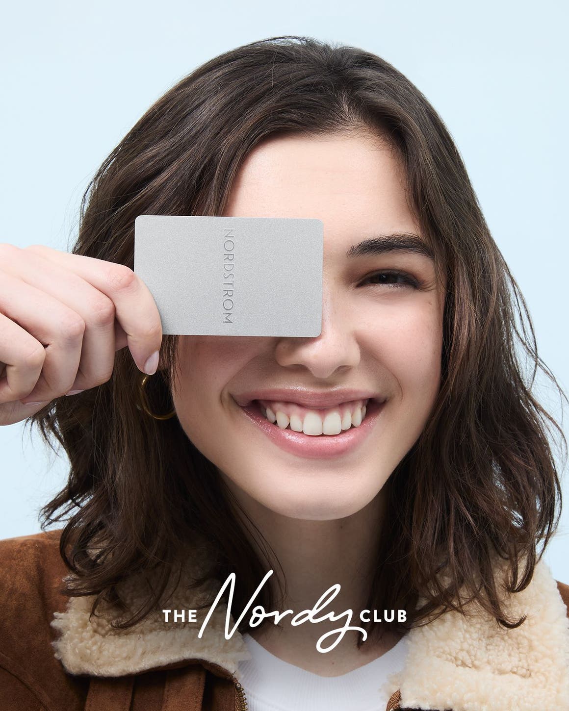 A woman smiling and holding up a Nordstrom card. 