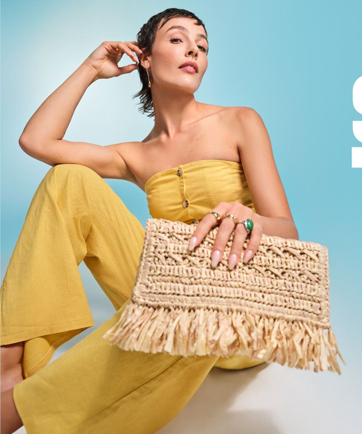 A woman wearing a yellow top and pants and holding a straw bag.
