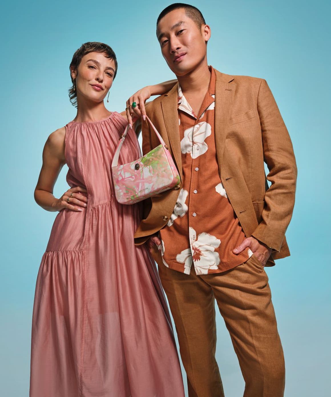 A woman wearing a pink tiered halter dress and a man wearing a floral shirt and tan suit.